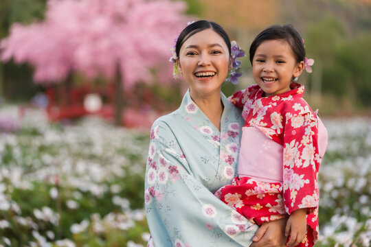 woman and child girl in yukata (kimono dress) with sakura flower or cherry blossom blooming in garden