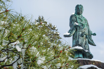 兼六園・冬の静寂：雪を纏う松の枝先と静かに佇む日本武尊像 / Winter Serenity in Kenrokuen: Snowy Pine Branches and the Silent Statue of Yamatotakeru © Taketo Miyajima
