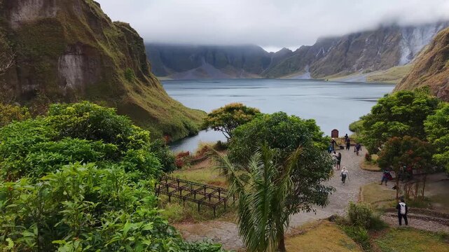 Pinatubo, philippines. Mountain lake lies within green hills. Lush trees frame the foreground. People stroll along a path. They look calm and content. Ideal for nature tourism or travel content