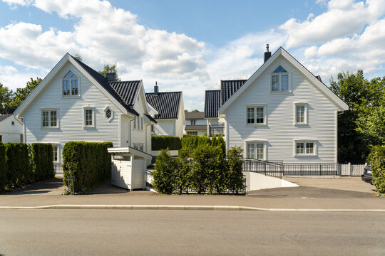 View of pristine white homes stand against a backdrop of lush green trees and a bright blue sky in Bygdoy, Oslo, Norway.