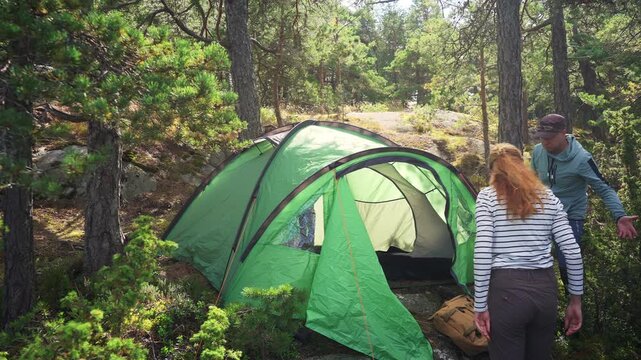 Couple setting up green tent in Finnish forest, outdoor camping scene with natural environment, focus on sustainable travel and respect for nature.
