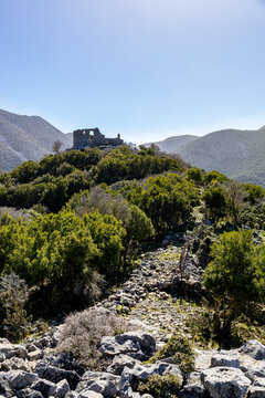 View of ancient ruins perched atop a verdant hill, amidst a landscape of rugged terrain under a clear azure sky, Askifou, Chania, Greece.