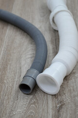 Flexible drain pipes for sink or washing machine placed on wooden floor. Household plumbing parts for water drainage, repair and home maintenance.