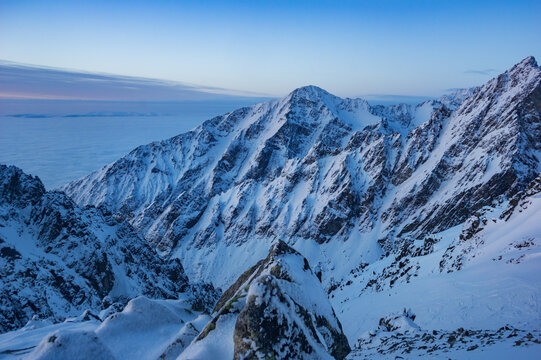 View of jagged, snow-laden peaks pierce through the crisp morning air, casting long shadows across the pristine white landscape, Vysoke Tatry, Presovsky kraj, Slovakia.