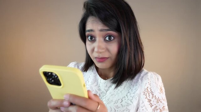 Close up of sad unhappy young Asian girl woman hold phone look at camera nodding head negative feels nervous, online network problems, isolated over grey studio background.