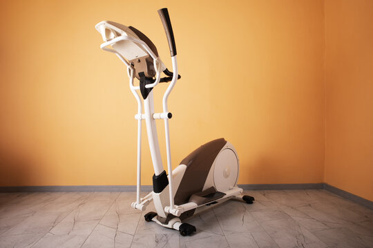 Sleek elliptical exercise machine in a minimal home interior with orange wall and marble floor, perfect for fitness and healthy lifestyle concepts.