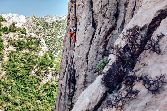 View of a climber ascends a sheer cliff face, set against a breathtaking backdrop of green forest and distant snow-capped peaks, Starigrad, Zadar County, Croatia.