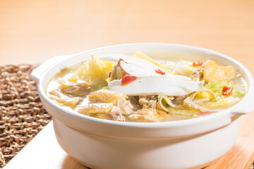 A white ceramic pot filled with chicken soup containing fish maw, chicken pieces, and Chinese herbs in clear broth
