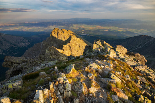 View of jagged peaks bathed in the warm glow of the setting sun, casting long shadows across the rugged terrain, a majestic natural vista, Vysoke Tatry, Slovakia.