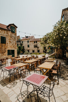 View of an outdoor cafe bathed in sunlight, tables and chairs awaiting patrons amidst the stone buildings, creating a tranquil scene, Stari Grad, Croatia.