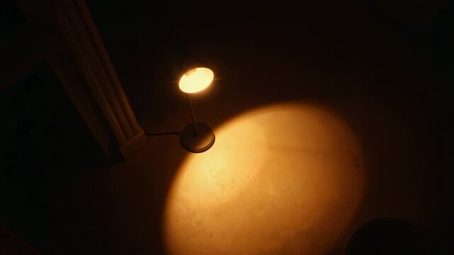 Desk lamp tilting shade and camera panning, shifting warm circular floor light for lighting study