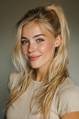 Naklejka premium Young woman smiles softly with light hair in a high ponytail, shot in warm lighting with a neutral background