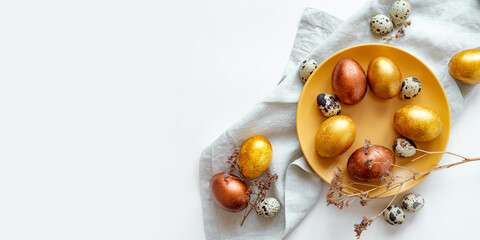 Golden and bronze Easter eggs in a orange plate on a linen napkin on a white background
