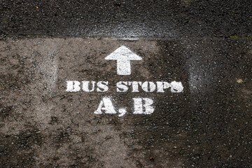Bus stop and route direction marking painted on wet asphalt road surface. Urban transportation concept featuring directional arrow, road text, and textured pavement background. 