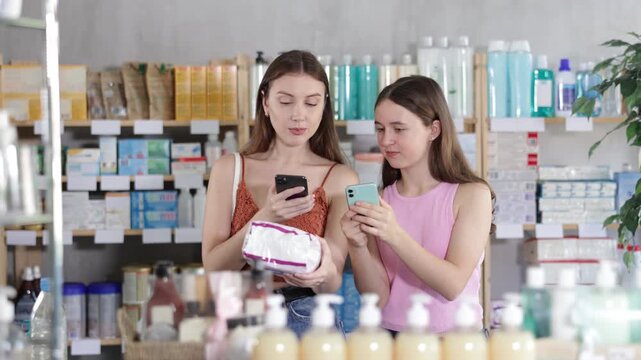 Near display case in pharmacy, mom and daughter scans barcode on feminine pads, reads user manual. Client studies product in detail, collects information online.