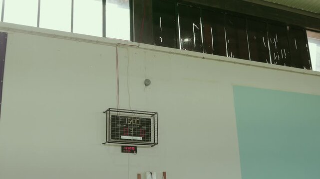 Electronic scoreboard with timer mounted on indoor gym wall