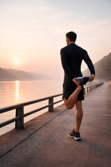 Fototapeta premium Man in athletic apparel performing a leg stretch on a scenic pier overlooking calm water during a colorful sunrise, focusing on morning fitness and well being