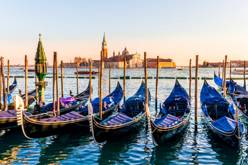 row of parked venetian gondola boats in Grand canal of Venice. Beautiful sunset or sunrise landscape with gondolas in blue water of Venice. © Yaroslav
