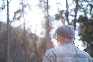 A man with a hat from behind walking through the forest with lens flare 