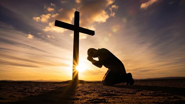 Silhouette of a Man Kneeling in Prayer Before a Cross at Sunset