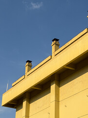Minimalist yellow building facade with chimneys against blue sky
