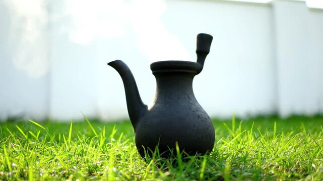 A black teapot sits on a grassy lawn with a white wall in the background, captured from multiple angles with consistent lighting anding. The teapot's shape is round with a curved spout and handle.