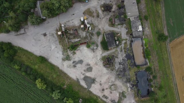 Aerial view of decaying industrial complex surrounded by farmland. Useful for depicting economic decline, environmental impact, rural industrialization, or post-war scenes.