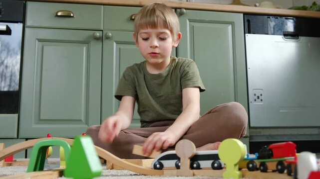 Cute little blonde child boy sitting on the floor playing with wooden toy train. Toddler kid plays railway. Made of natural materials. Birthday gift. Preschool employment. Brain, coordination exercise
