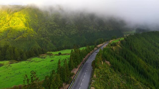 Road trip in the Azores, a drone shot of a car moving down the road on Sao Miguel island in ush green scenery with volcanic mountains, travel in Portugal