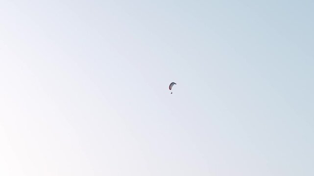 Single powered paraglider flying through vast pastel sky high above distant countryside horizon. Paramotoring pilot drifting slowly in open air minimal composition extreme aerial activity. Adventure