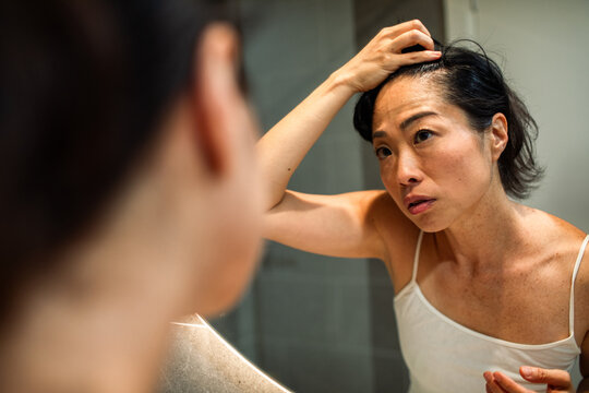 Mature woman checking scalp for hair loss in bathroom mirror