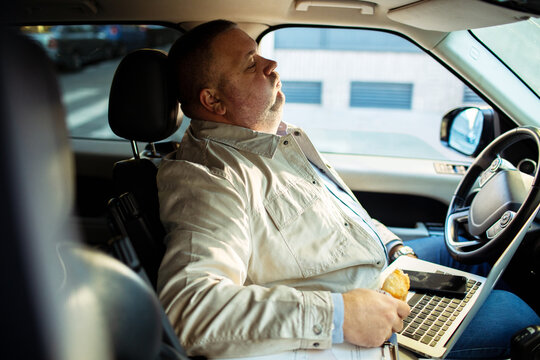 Tired businessman resting with laptop in parked car