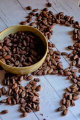 Fototapeta premium Rustic still life of natural cocoa beans in a handcrafted ceramic bowl, placed on a white wooden surface with scattered seeds around it