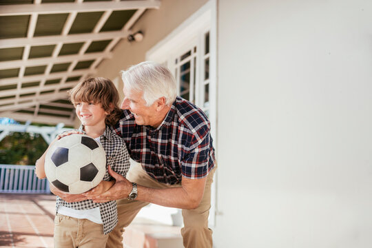 Grandfather helping grandson with soccer ball on home porch