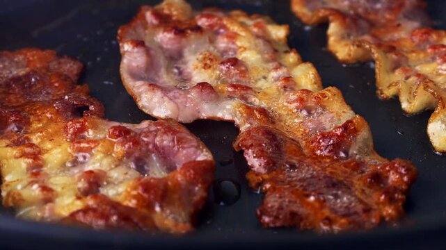 Slices of bacon frying in black pan closeup