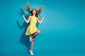 Cheerful young woman in a yellow dress jumping against a bright blue background with a vibrant and...