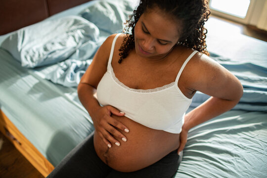Expectant mother holding belly on bed at home