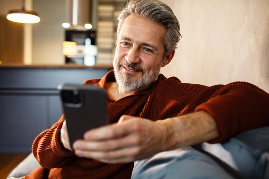 Smiling middle-aged man using smartphone at home