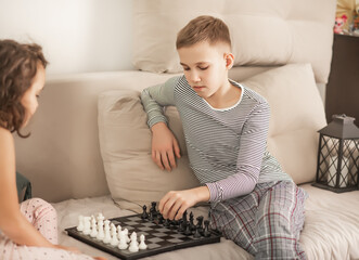 Two children playing chess on a cozy bed at home, focused and thoughtful during a quiet indoor activity.