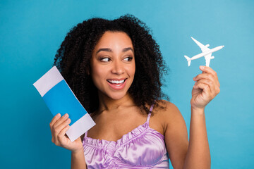 Young woman smiles holding a travel envelope and toy airplane against a blue backdrop suggesting...