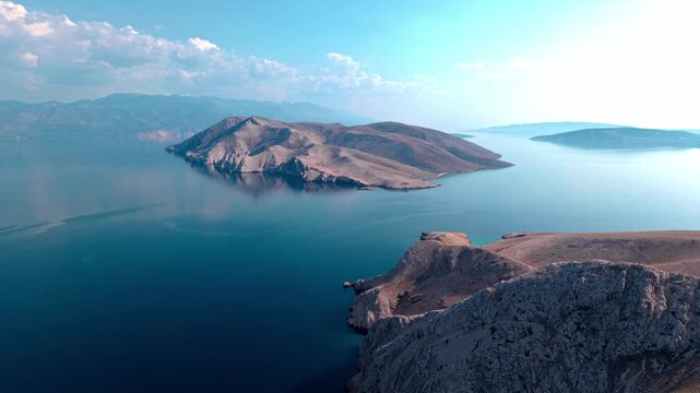 Aerial panoramic view of Prvić island in the Adriatic Sea near Krk, Croatia. Rocky barren landscape surrounded by deep blue water and distant mountain coastline