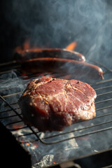 Close up of raw steak and sausages on a metal grill with smoke and fire glow, ideal for barbecue cooking, outdoor food, and summer grilling concepts.