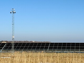 Fototapeta premium Solar panel installation in an open field with dry grass and a tall light pole under clear sky.