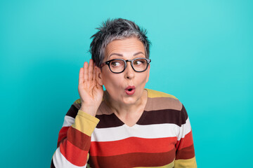 Older woman with short gray hair and glasses listens closely against a blue studio background...