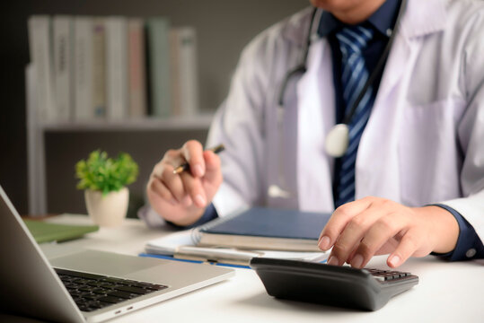 doctor using calculator and laptop for medical cost calculation, health insurance billing, and hospital budget management in clinic office. High quality healthcare financial concept.