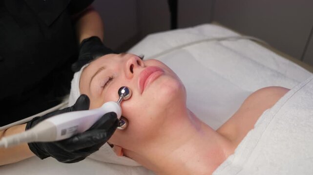 Cosmetologist performing an electric facial massage with a microcurrent device on a woman's cheek