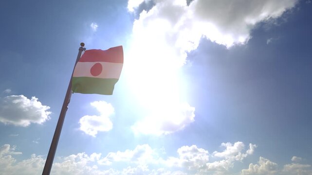 Niger Flag waving on a Flagpole from a Moving Angle in front of a blue sky with clouds	