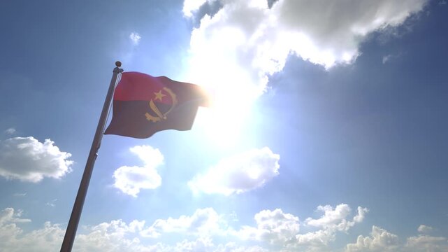 Angola Flag waving on a Flagpole from a Moving Angle in front of a blue sky with clouds	