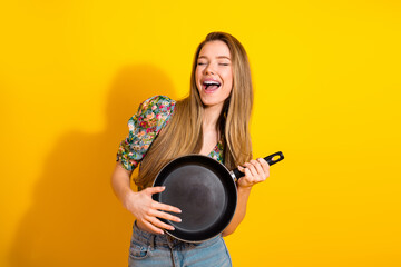 Young woman with frying pan smiling against bright yellow background lifestyle photo