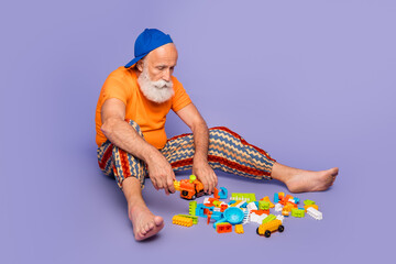 Fototapeta premium Carefree elderly man plays with colorful blocks on a purple background, wearing orange shirt and striped pants